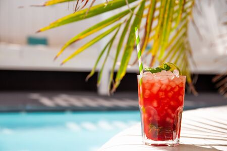 fresh tasty cocktail near swimming pool and tropical palm leaves in summer