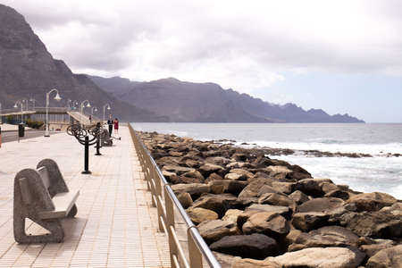 AGAETE, LAS PALMAS - OCTOBER 17, 2019: seafront with street lights and benches near Atlantic ocean, mountain in clouds in Agaete, Las Palmasのeditorial素材