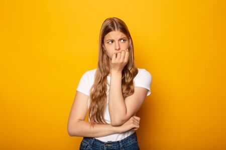 worried blonde girl with long hair looking away isolated on yellow backgroundの写真素材