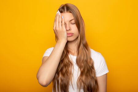 tired blonde girl with hand on face isolated on yellowの写真素材