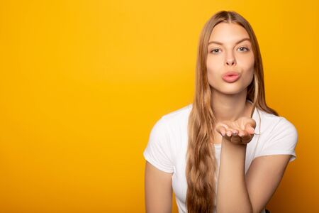 blonde girl blowing kiss at camera isolated on yellowの写真素材