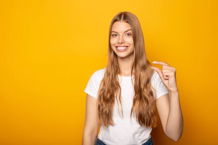 smiling blonde girl showing small gesture isolated on yellowの写真素材