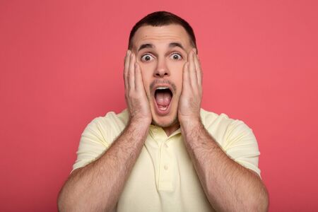 scared adult man screaming and touching face on pink background