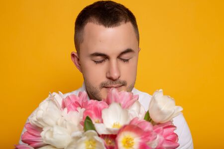 man with closed eyes smelling bouquet of flowers on yellow backgroundの写真素材