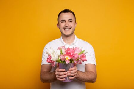 smiling man holding bouquet of flowers on yellow backgroundの写真素材