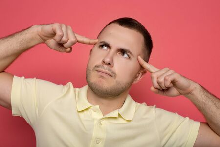 pensive man touching head and looking away on pink background