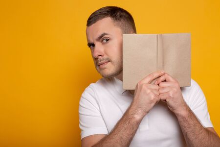 man holding book near face on yellow background