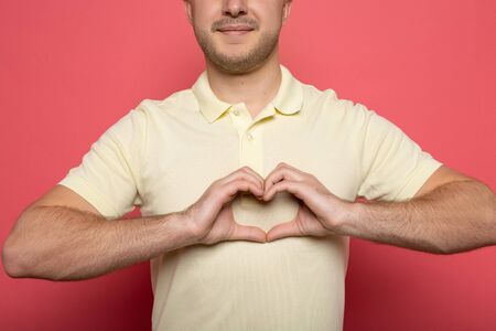 cropped view of smiling man showing heart gesture on pink backgroundの写真素材