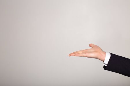 cropped view of young businessman in black suit pointing with hand on grey background