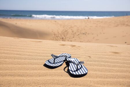 selective focus of striped flip flops on sand hills near Atlantic ocean against clear blue sky at sunny day in Maspalomas, Gran Canariaの写真素材