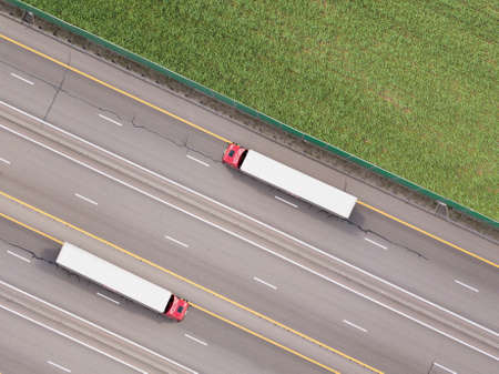 Dump trucks carrying goods on the highway. Red truck driving on asphalt road along the green fields. seen from the air. Aerial view landscape. drone photography. cargo deliveryの写真素材