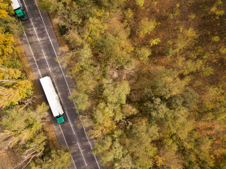 Dump trucks carrying goods on the highway. Greeen trucks driving on asphalt road along the forest seen from the air. Aerial view landscape. drone photography. cargo deliveryの写真素材