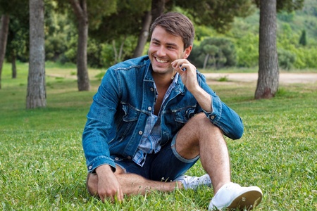 a happy young man in a park sitting on the grassの写真素材