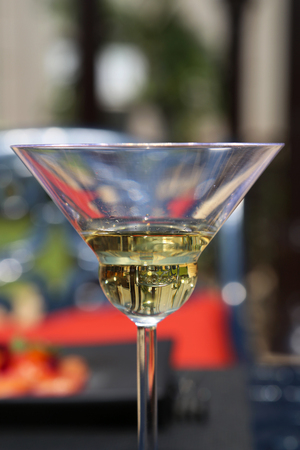 A Glass of Martini at Daytime atop Black Ornamented Metal Table with a Black metal Ornamented Chair and a Red Pillow in the Backgroundの写真素材