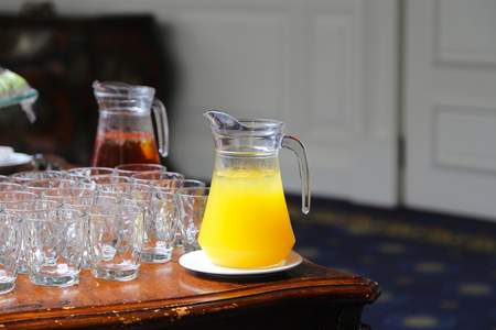 Two Glass Jars of Orange and Apple Juice next to Empty Glasses Set for a Coffee Break Catering Eventの写真素材