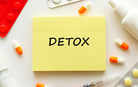 Notepad with text DETOX on a white background. Nearby are various medicines. Medical concept.