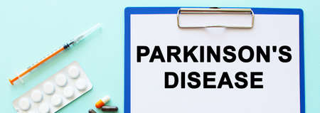 A clipboard with paper lies on a table near drugs and a syringe. Inscription PARKINSONS DISEASE. Medical concept.の写真素材