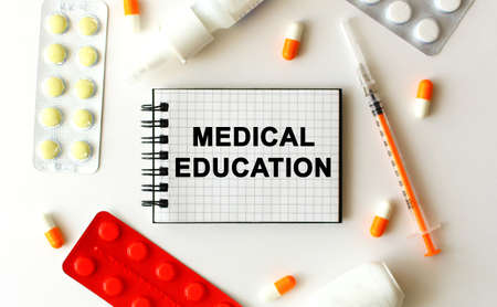 Notepad with text MEDICAL EDUCATION on a white background. Nearby are various medicines. Medical...