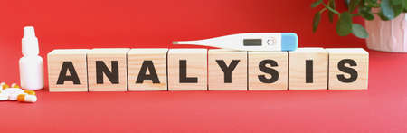 The word ANALYSIS is made of wooden cubes on a red background with medical drugs.の写真素材