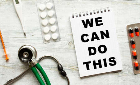 WE CAN DO THIS is written in a notebook on a white table next to pills and a stethoscope. Medical conceptの写真素材