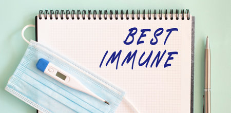 A medical protective mask and a thermometer are on the notebook. BEST IMMUNE text in a notebook.