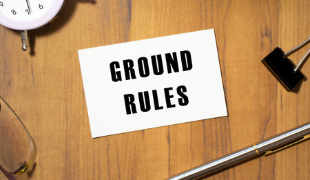 A business card with the text GROUND RULES lies on a wooden office table among office supplies. Business concept.の写真素材