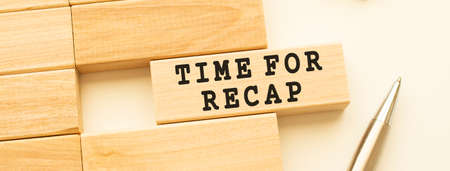 TIME FOR RECAP text on a strip of wood lying on a white table with a metal pen. Concept.の写真素材