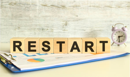 Wooden cubes lie on a folder with financial charts on a gray background. The cubes make up the word RESTART. Business concept.の写真素材
