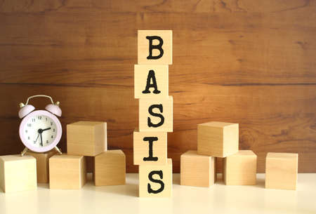 Five wooden cubes stacked vertically to form the word BASIS on a brown background. Cubes are scattered nearby and there is a clock. Front View Conceptsの写真素材