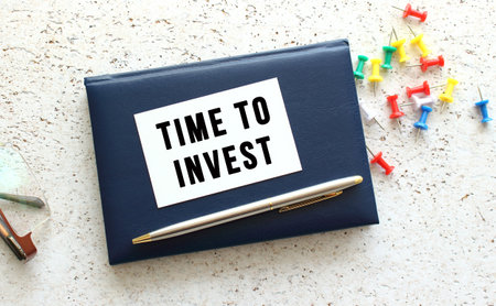 Text TIME TO INVEST on a business card lying on a blue notebook next to the glasses. Business concept.の写真素材