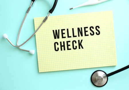 The text WELLNESS CHECK is written in a yellow pad that lies next to the stethoscope on a blue background. Medical conceptの写真素材