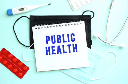 The text PUBLIC HEALTH is written on a white sheet of notepad that lies on a blue background next to a thermometer and medical face masks. Medical conceptの写真素材