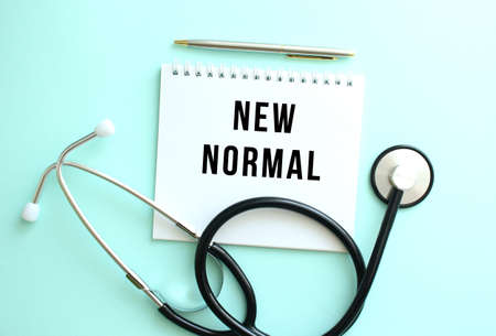 White notepad with the words NEW NORMAL and a stethoscope on a blue background.の写真素材