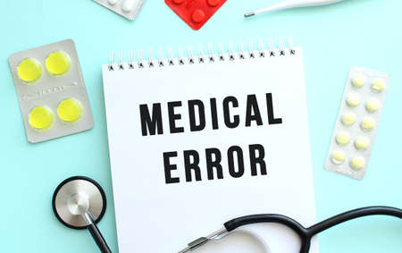 The text MEDICAL ERROR is written in a notebook that lies next to the stethoscope, medicine on a blue background. Medical conceptの写真素材