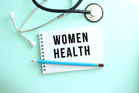 White notepad with the words WOMEN HEALTH and a stethoscope on a blue background. Medical concept
