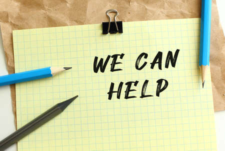 WE CAN HELP lettering on a yellow sheet of paper over crumpled kraft paper. Pencils and paper clip. Business concept.の写真素材