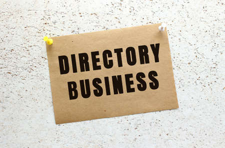 A sheet of craft paper with DIRECTORY BUSINESS text attached to a white textured wall with a button. Office reminder. Business concept.の写真素材