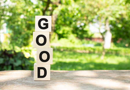 Wooden cubes are stacked vertically on a wooden table in the garden. The word GOOD is written in black letters. Concept for your designの写真素材