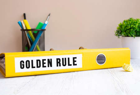 A yellow folder labeled GOLDEN RULE is on the office desk. Flower and stationery background. Financial concept.の写真素材