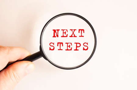 A man's hand holds a magnifying glass. Close-up of the NEXT STEPS text. Light background.の写真素材