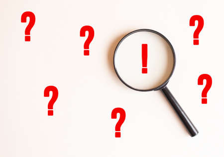 A magnifying glass on a pale beige background with an exclamation mark. Magnifier with exclamation mark. View from above.の写真素材