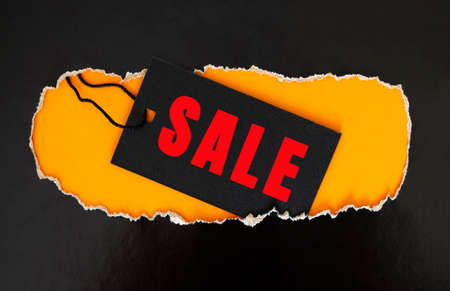 A black rectangular clothing tag rests on torn black paper. Yellow background.の写真素材