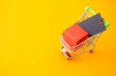 Gift box with a red bow in a metal shiny shopping trolley on wheels on a yellow background.の写真素材