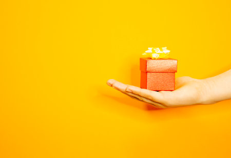 The girls hand is holding a beautiful gift box. Makes a gift. Yellow background.