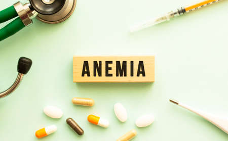 The word ANEMIA on a wooden cube with a stethoscope and pills. Medical concept. Flat lay.の写真素材
