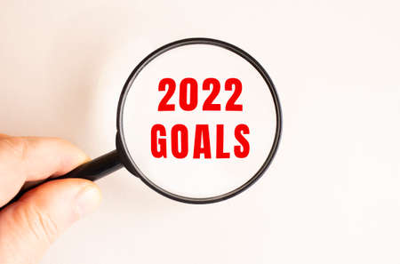 A man's hand holds a magnifying glass. Close-up of the 2022 GOALS text. Light background.の写真素材