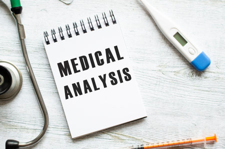 MEDICAL ANALYSIS is written in a notebook on a light wooden table next to a stethoscope. Medical conceptの写真素材