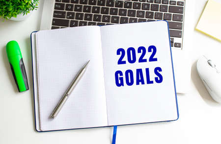 Modern white office desk with laptop and other accessories. Creative flat lay photo of workspace desk. Notepad with the text 2022 GOALS in the middle. View from above.の写真素材
