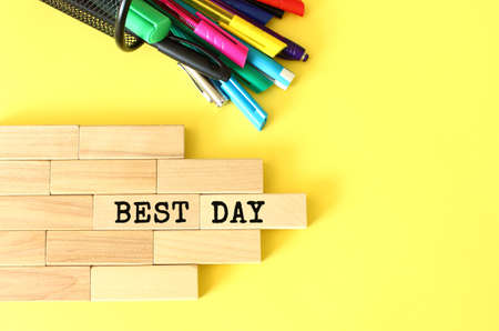 Wooden blocks stacked next to pens and pencils on a yellow background. BEST DAY text on a wooden block.の写真素材