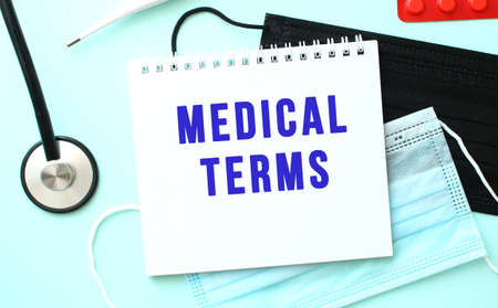 The blue text MEDICAL TERMS is written in a notebook that lies on a blue background next to a medical masksの写真素材